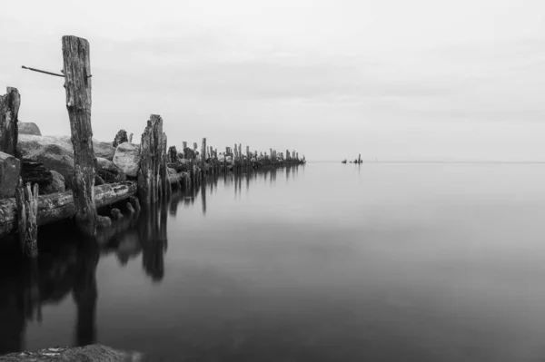 石と木の脚でできた古い桟橋は金属製のネジで残され水面は穏やかです — ストック写真