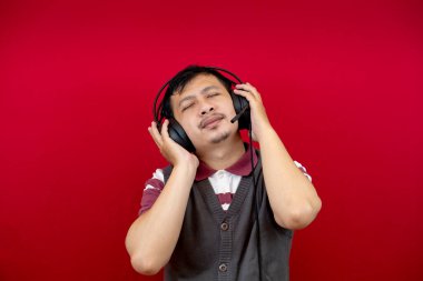 Yakışıklı bir Asyalı, kulaklık kullanarak şarkı dinlerken eğleniyor ve dans ediyor. kırmızı arkaplan. 