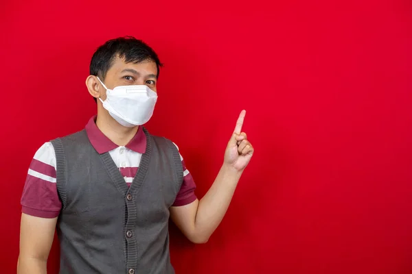 Maskeli sağlıklı yakışıklı Asyalı genç adam kırmızı afiş arkaplanını işaret ederek fotokopi alanı ile izole etti.. 