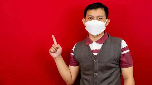 Maskeli sağlıklı yakışıklı Asyalı genç adam kırmızı afiş arkaplanını işaret ederek fotokopi alanı ile izole etti.. 