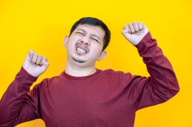 Kırmızı gömlek giyen Asyalı adam vücudunun ağrıdığını ifade ediyor. Sarı arkaplan. 