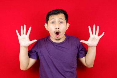 Asyalı adam abartılı yüz ifadelerine şaşırdı ve şok oldu. Kırmızı arka planlı fotoğraf stüdyosu. 