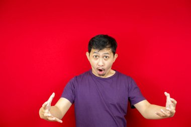 Mor tişört giyen sinirli Asyalı adamın portresi. kırmızı arkaplan. 