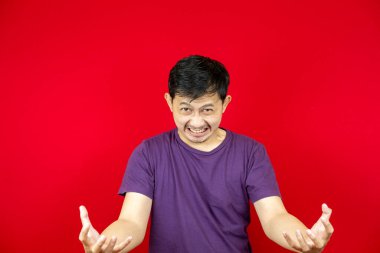 Mor tişört giyen sinirli Asyalı adamın portresi. kırmızı arkaplan. 