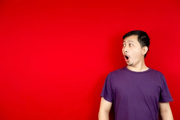 Asyalı adam şaşırmış bir yüzle içerik için boş bir yer gösterdi. Reklam modeli konsepti. kırmızı arkaplan. 