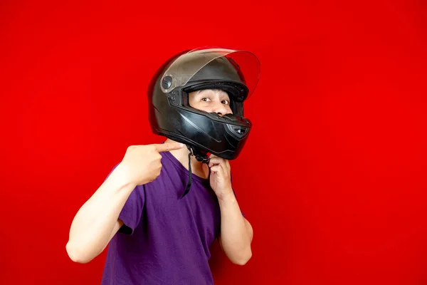 Kafasına kask takan Asyalı adam onu takmak için kask askısını gösteriyor. kırmızı arka plan fotoğraf stüdyosu.