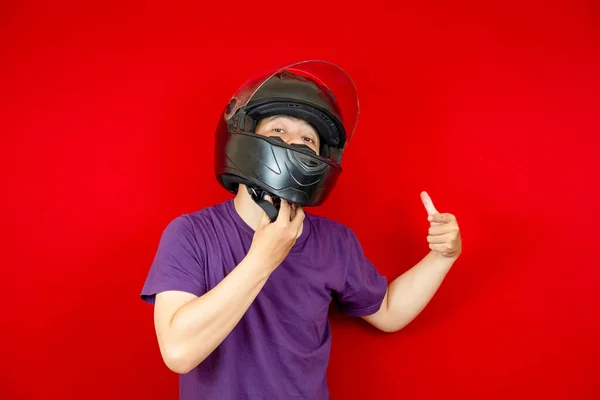 Kafasına kask takan Asyalı adam onu takmak için kask askısını gösteriyor. kırmızı arka plan fotoğraf stüdyosu.