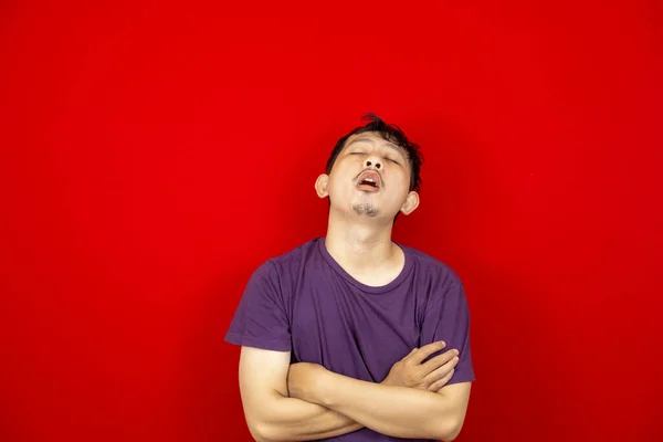 Kendini tembel ve uykulu hisseden Asyalı bir gencin stüdyo portresi. kırmızı arkaplan. 