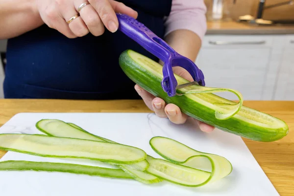 Kadınların elleri bir salatalığı bir Peeler bıçağıyla kesiyor.