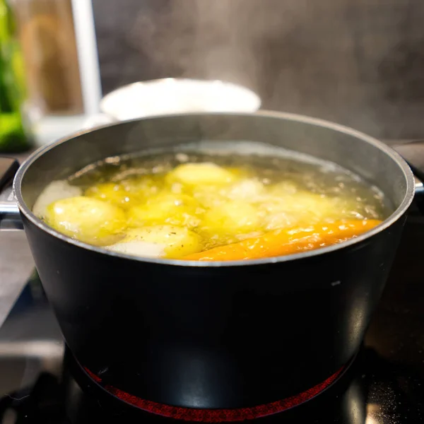 Pot of boiling water in which potatoes and carrots are boiled — Stock Photo, Image
