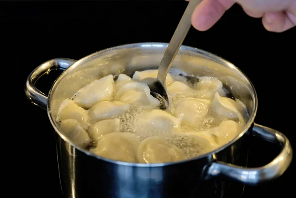 Knödel mit einem Löffel in einem Topf mit kochendem Wasser gemischt. Gekochte Knödel in einer Pfanne. schwarzer Hintergrund — Stockfoto