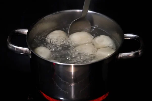 Khinkalları kaynar suda pişirmek. Tavada haşlanmış khinkali. Aşçı köfteleri kaşıkla karıştırır..