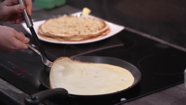 The woman turns the pancake over in the pan. Crepes are fried in a pan. homemade Russian blini baking process. Cooking smoke goes up from pancake. slow motion video — Stock Video