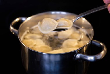 Hamur köfteleri bir kaşık dolusu kaynar suya karıştırılmış. Tavada kaynamış hamur köftesi. siyah arkaplan