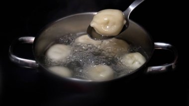 Khinkalları kaynar suda pişirmek. Tavada haşlanmış khinkali. Aşçı köfteleri kaşıkla karıştırır..