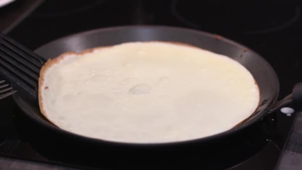 Die Frau dreht den Pfannkuchen in der Pfanne um. Crêpes werden in einer Pfanne gebraten. hausgemachtes russisches Blini-Backen. Kochrauch steigt aus Pfannkuchen auf. Zeitlupenvideo — Stockvideo