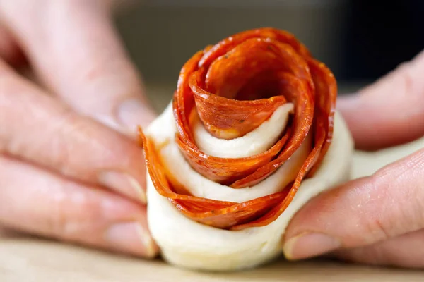La mujer está haciendo un bocadillo de pepperoni en forma de rosa. Pastelería con salami. hojaldre casero listo para hornear. —  Fotos de Stock