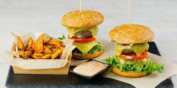 İki büyük burger ve siyah taş tabakta izole edilmiş tatlı patates. hafif tahta arkaplan
