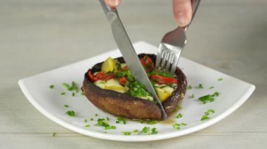 Doldurulmuş Portobello mantarı. Kadın bıçakla keser ve domates ve mozzarella ile doldurulmuş şampiyonların tadına bakar..