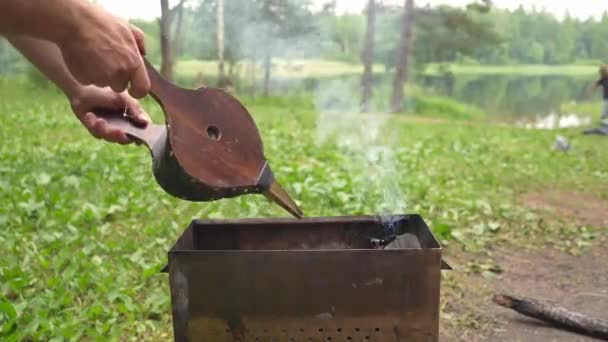 Un hombre sopla un fuego con el fuelle de chimenea de madera dura en la barbacoa. Descanse en el bosque en un viaje de pesca junto al lago. — Vídeos de Stock