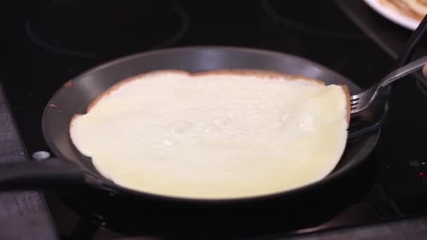 Η γυναίκα γυρίζει την τηγανίτα στο τηγάνι. Οι κρέπες τηγανίζονται σε τηγάνι. σπιτική ρωσική διαδικασία ψησίματος blini. Το μαγείρεμα καπνού ανεβαίνει από την κρέπα. βίντεο αργής κίνησης — Αρχείο Βίντεο