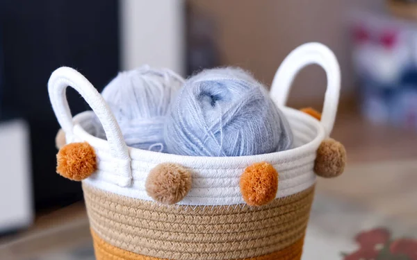 Hasır sepetin üst görüntüsü, el örgü için yün yumakları, eski ahşap bir masa üzerinde kancalar ve örgü iğneleri..