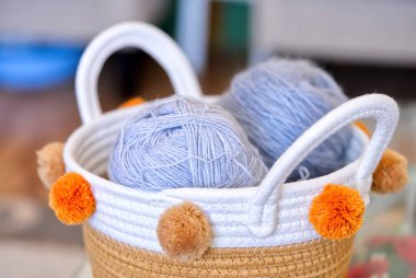 Elle örgü örmek için yün yumakları, eski ahşap bir masanın üzerinde kancalar ve örgü iğneleri olan hasır bir sepetin üst görüntüsü. Kapat.