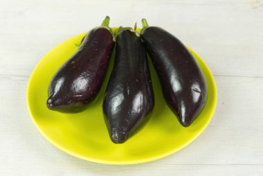 Işık masasında 3 patlıcan. Yeşil bitkide taze çiğ Mor Patlıcan. Kapat.