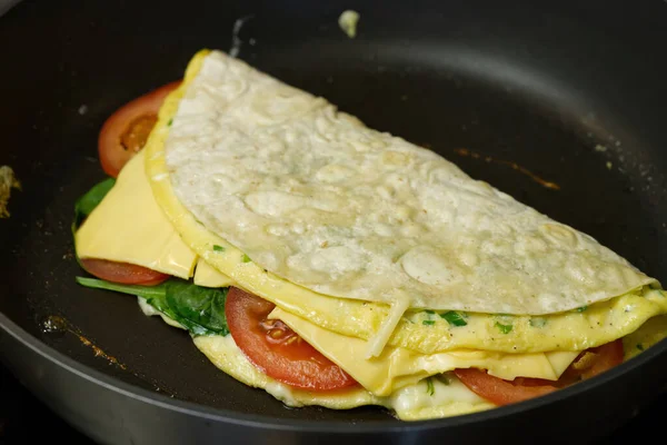 Pita wrap with tomatoes, cheese, ham and spinach on the frying pan. close up