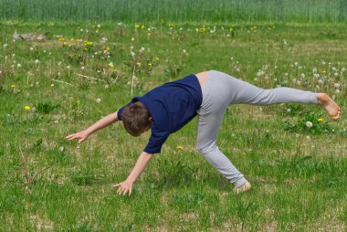 Çocuk akrobatik tekerlek yapıyor. Çimlerin üzerinde. Kapat.