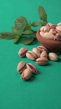 Yeşil yapraklar ve kahverengi kâseyle süslenmiş fıstıklar. Yeşil arka plan, üst manzara. Düz yatıyordu.