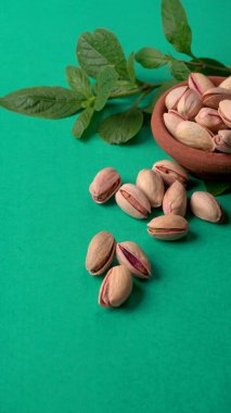 Yeşil yapraklar ve kahverengi kâseyle süslenmiş fıstıklar. Yeşil arka plan, üst manzara. Düz yatıyordu.