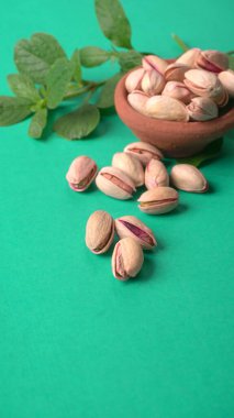 Yeşil yapraklar ve kahverengi kâseyle süslenmiş fıstıklar. Yeşil arka plan, üst manzara. Düz yatıyordu.