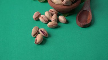 Yeşil yapraklar ve kahverengi kâseyle süslenmiş fıstıklar. Yeşil arka plan, üst manzara. Düz yatıyordu.