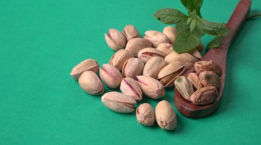 Yeşil yapraklar ve kahverengi tahta kaşıkla süslenmiş Pistachios veya Pista fındıkları. Yeşil arka plan, üst manzara. Düz yatıyordu.
