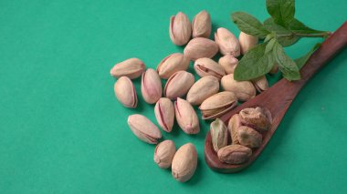 Yeşil yapraklar ve kahverengi tahta kaşıkla süslenmiş Pistachios veya Pista fındıkları. Yeşil arka plan, üst manzara. Düz yatıyordu.