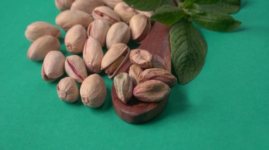 Yeşil yapraklar ve kahverengi tahta kaşıkla süslenmiş Pistachios veya Pista fındıkları. Yeşil arka plan, üst manzara. Düz yatıyordu.