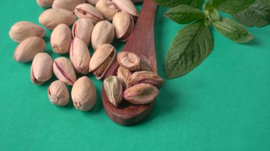 Yeşil yapraklar ve kahverengi tahta kaşıkla süslenmiş Pistachios veya Pista fındıkları. Yeşil arka plan, üst manzara. Düz yatıyordu.