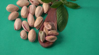 Yeşil yapraklar ve kahverengi tahta kaşıkla süslenmiş Pistachios veya Pista fındıkları. Yeşil arka plan, üst manzara. Düz yatıyordu.