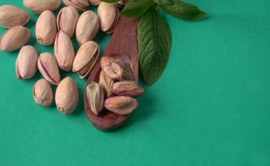 Yeşil yapraklar ve kahverengi tahta kaşıkla süslenmiş Pistachios veya Pista fındıkları. Yeşil arka plan, üst manzara. Düz yatıyordu.