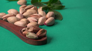 Yeşil yapraklar ve kahverengi tahta kaşıkla süslenmiş Pistachios veya Pista fındıkları. Yeşil arka plan, üst manzara. Düz yatıyordu.