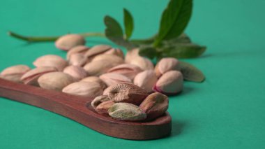 Yeşil yapraklar ve kahverengi tahta kaşıkla süslenmiş Pistachios veya Pista fındıkları. Yeşil arka plan, üst manzara. Düz yatıyordu.