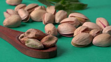 Yeşil yapraklar ve kahverengi tahta kaşıkla süslenmiş Pistachios veya Pista fındıkları. Yeşil arka plan, üst manzara. Düz yatıyordu.