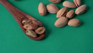 Yeşil yapraklar ve kahverengi tahta kaşıkla süslenmiş Pistachios veya Pista fındıkları. Yeşil arka plan, üst manzara. Düz yatıyordu.
