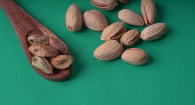 Yeşil yapraklar ve kahverengi tahta kaşıkla süslenmiş Pistachios veya Pista fındıkları. Yeşil arka plan, üst manzara. Düz yatıyordu.