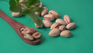 Yeşil yapraklar ve kahverengi tahta kaşıkla süslenmiş Pistachios veya Pista fındıkları. Yeşil arka plan, üst manzara. Düz yatıyordu.
