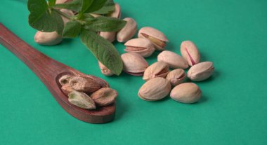 Yeşil yapraklar ve kahverengi tahta kaşıkla süslenmiş Pistachios veya Pista fındıkları. Yeşil arka plan, üst manzara. Düz yatıyordu.