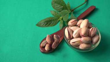 Yeşil yapraklar ve kahverengi tahta kaşıkla süslenmiş Pistachios veya Pista fındıkları. Yeşil arka plan, üst manzara. Düz yatıyordu.