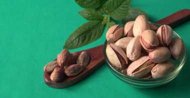 Kahverengi ahşap kaşık ve cam kavanozla süslenmiş fıstıklar veya Pista fındıkları. Yeşil arka plan, üst manzara. Düz yatıyordu.