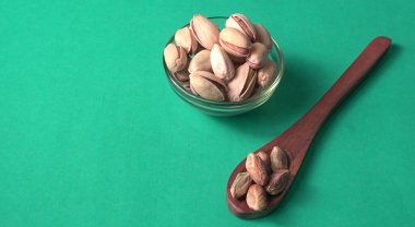 Kahverengi ahşap kaşık ve cam kavanozla süslenmiş fıstıklar veya Pista fındıkları. Yeşil arka plan, üst manzara. Düz yatıyordu.